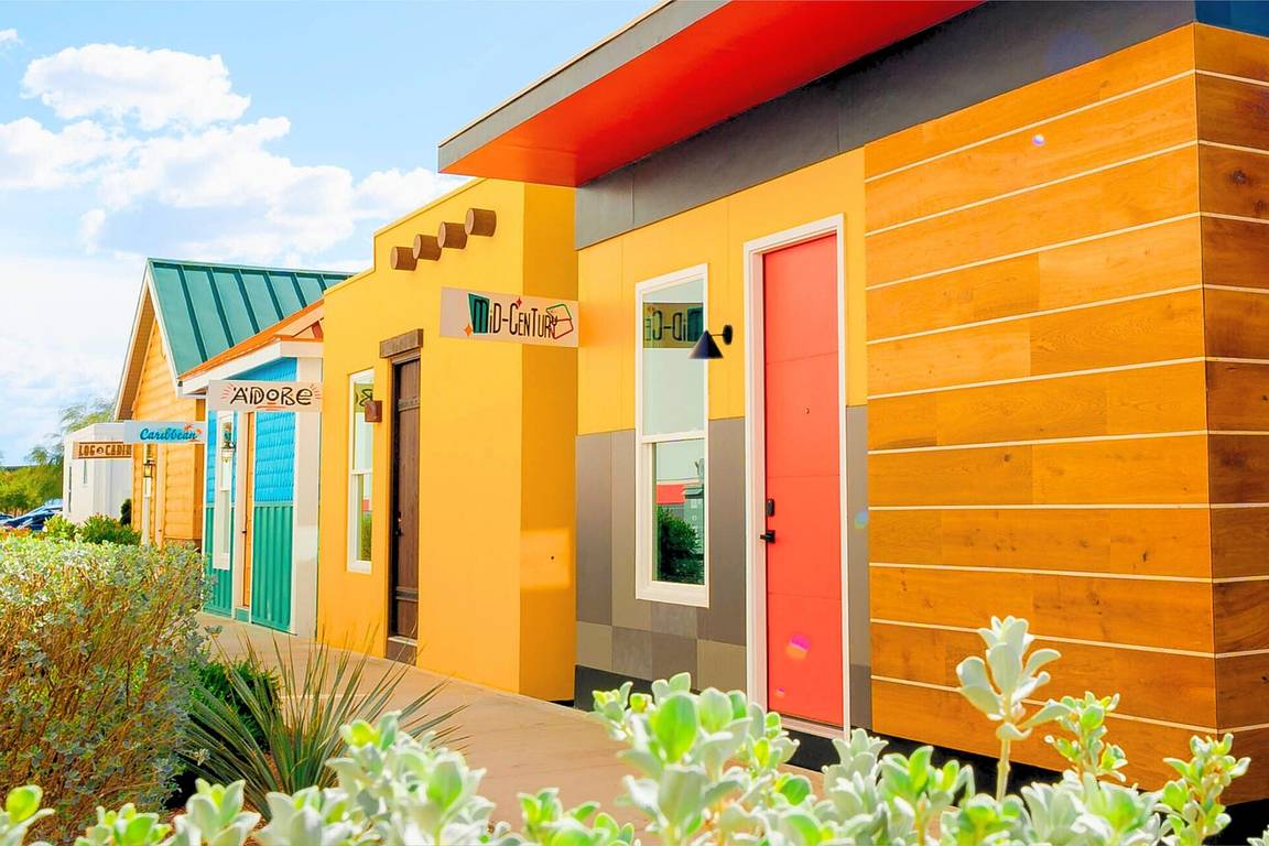 A row of small, colourful casita homes with wooden cladding and bright doors under a blue sky