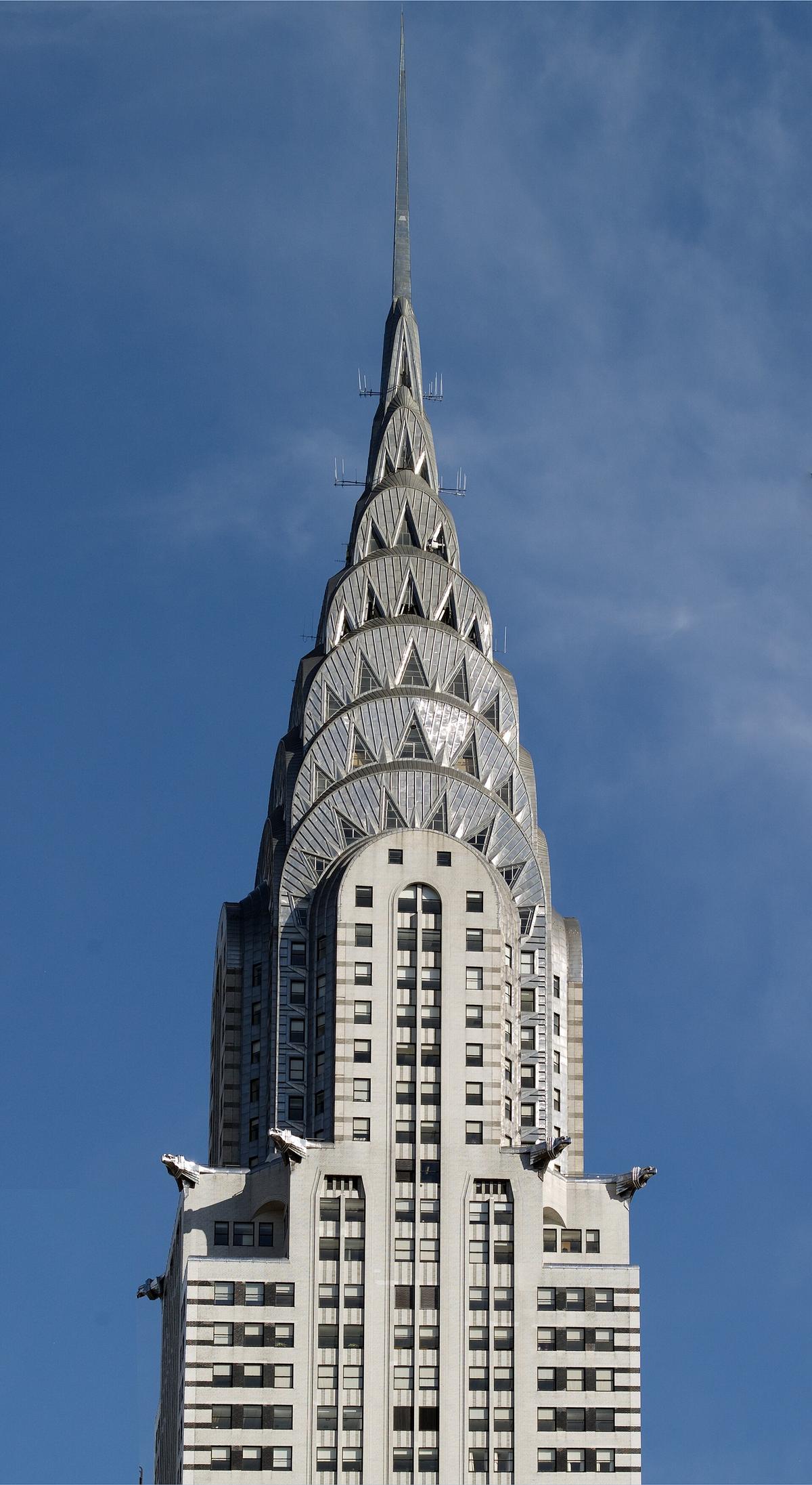 Close view of the Chrysler Building crown, its sunburst terraces and needle spire against blue sky