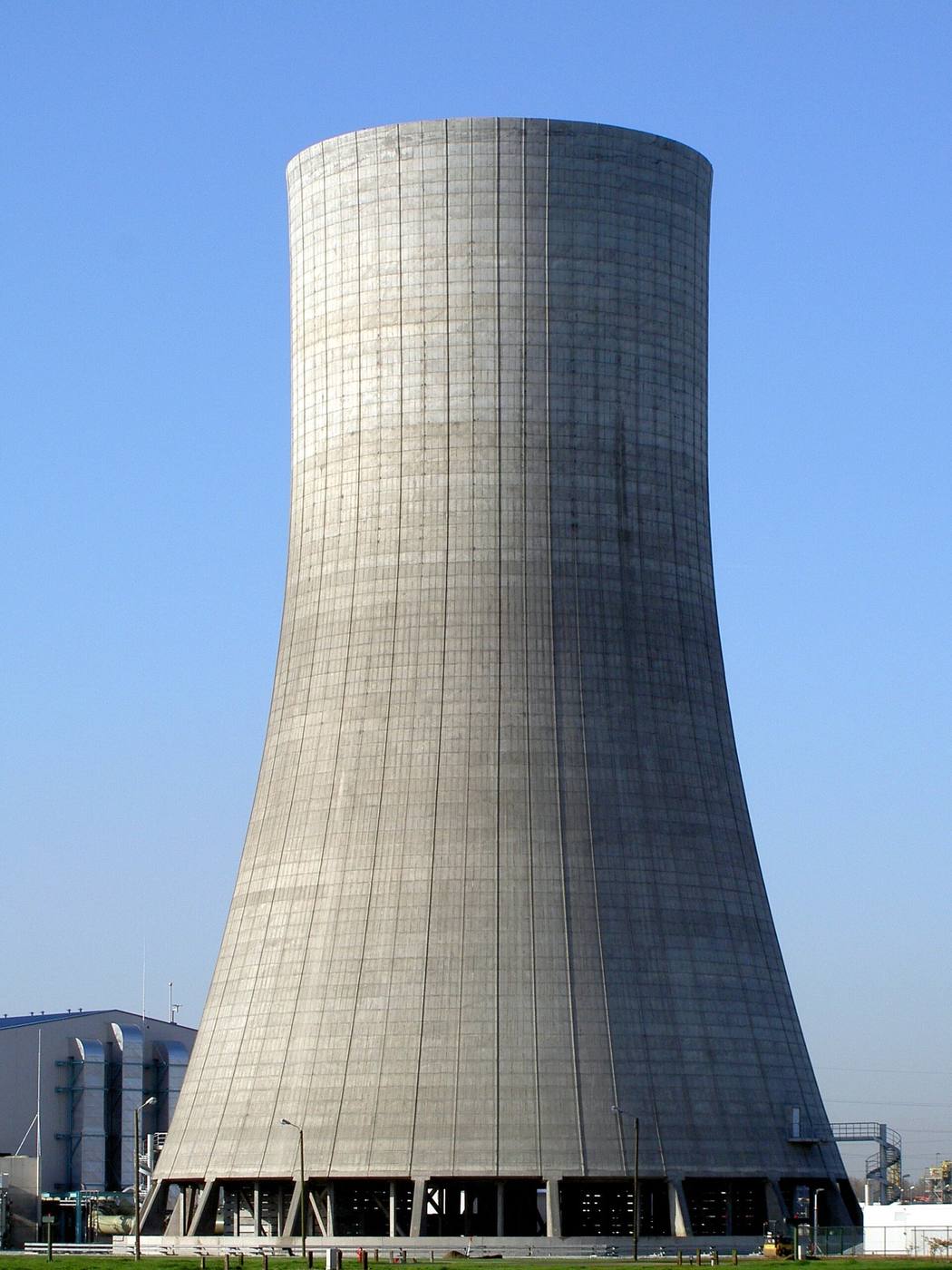A tall industrial cooling tower releasing vapour against the sky