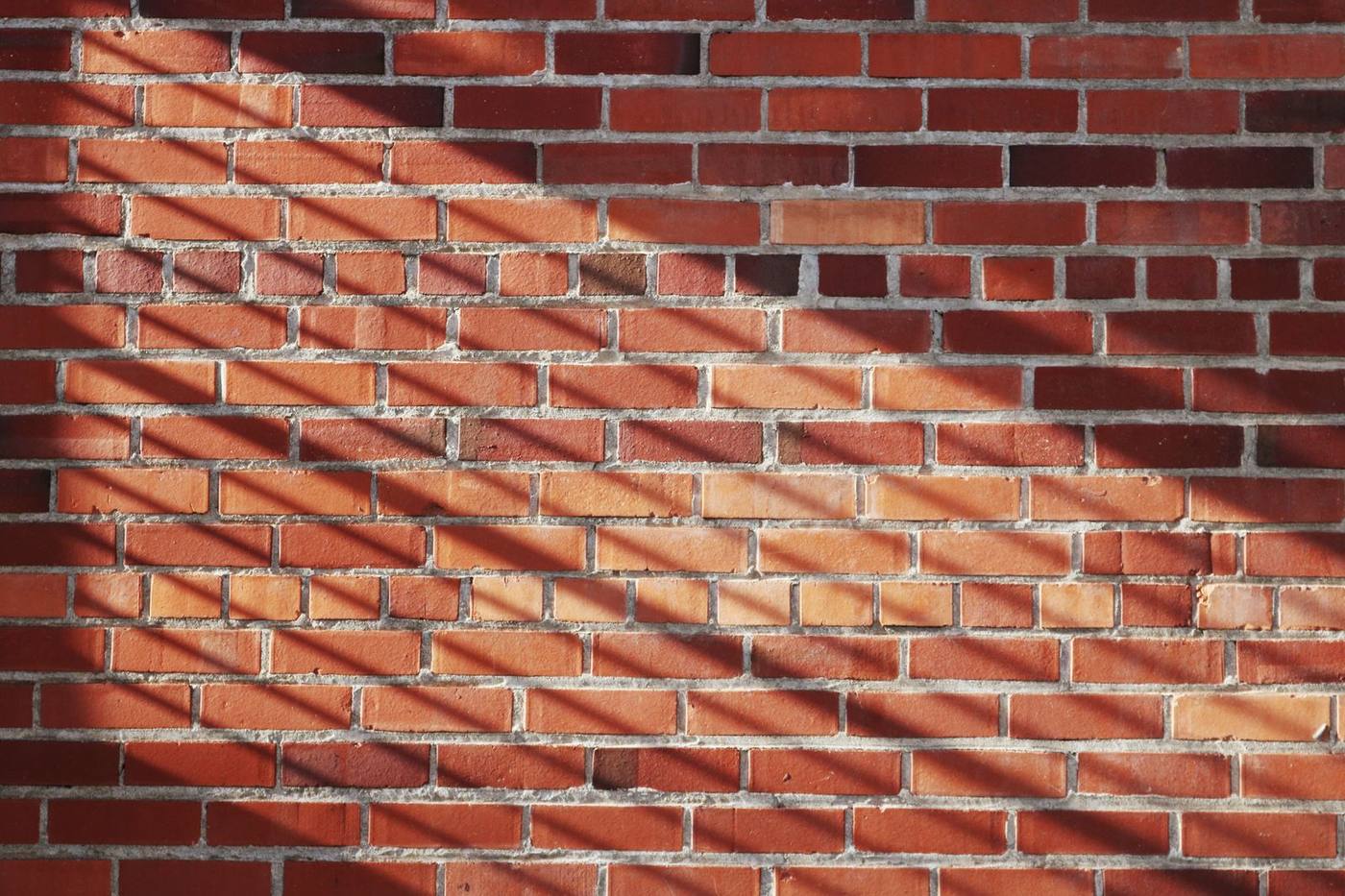 Red brick wall with striking shadows creating a textured pattern