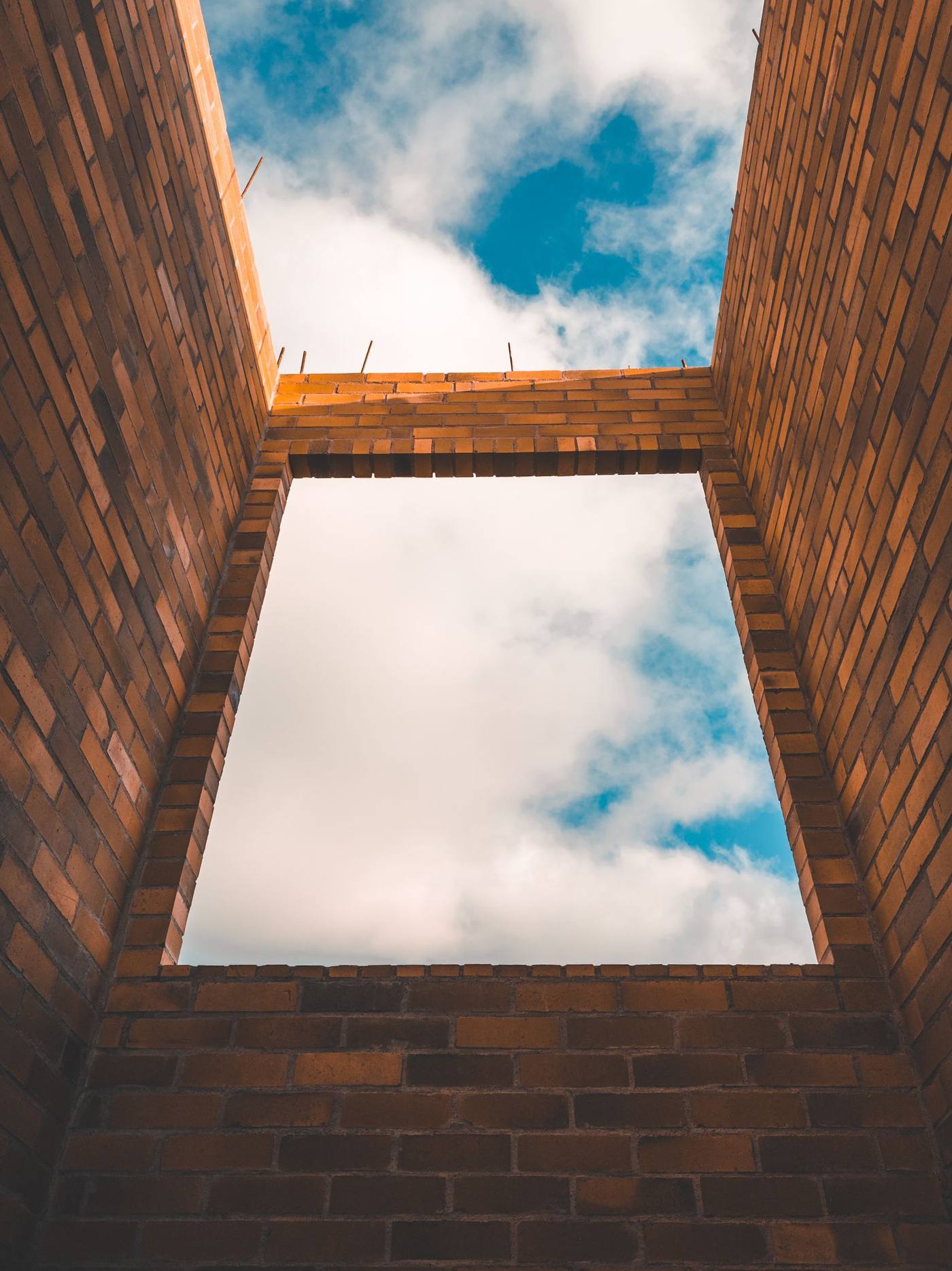 Low-angle view of an unfinished brick structure framing the cloudy sky
