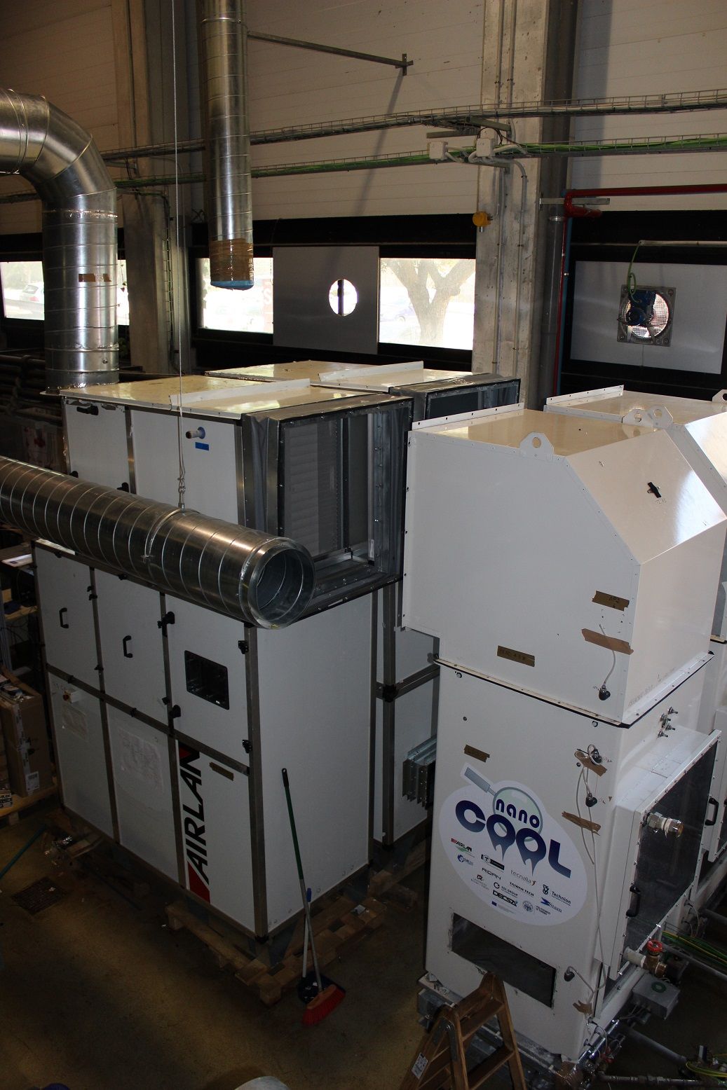 Large white air handling units with connected ductwork inside an industrial building