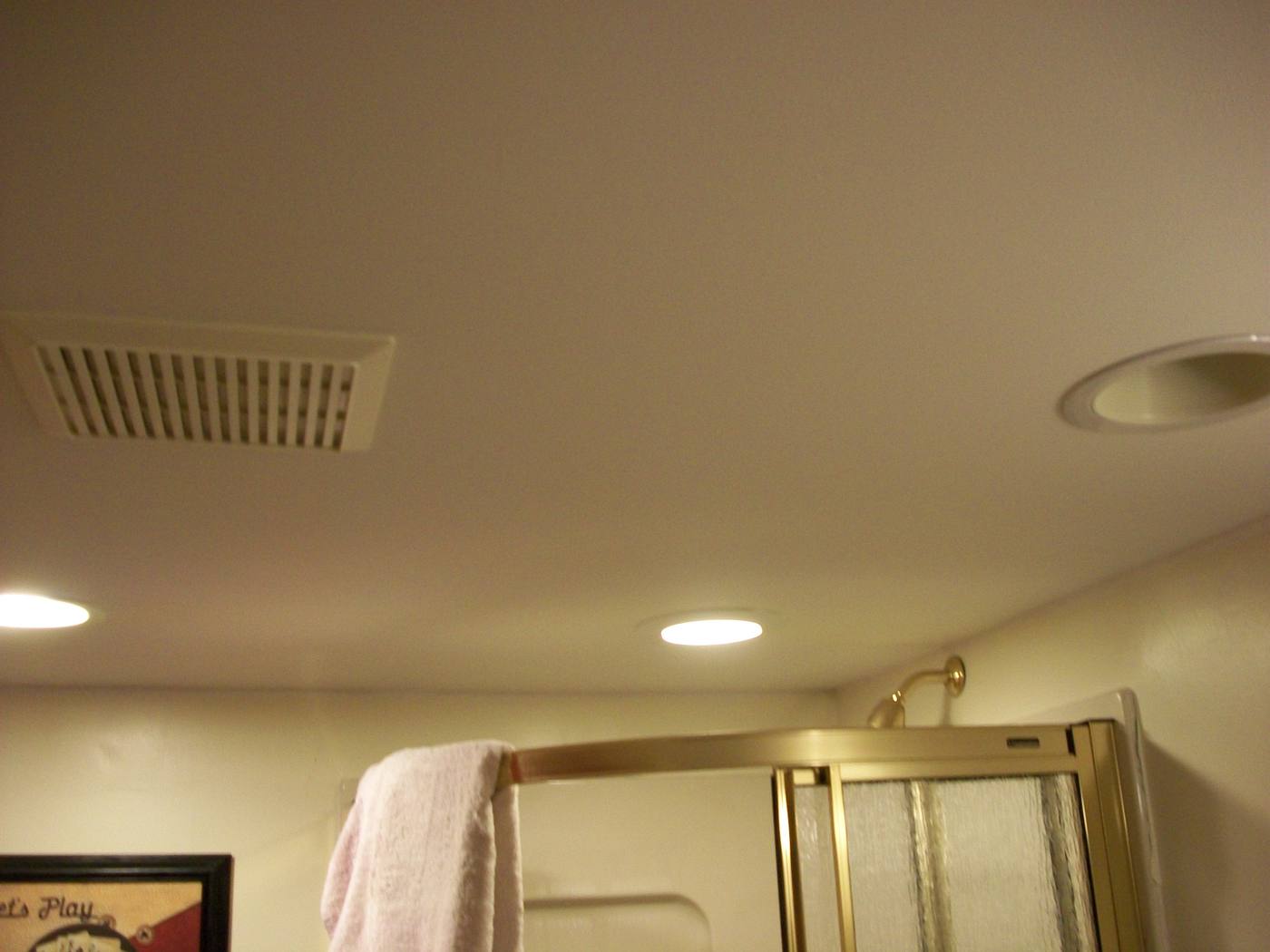 A ceiling vent grille in a bathroom interior, with a shower enclosure below