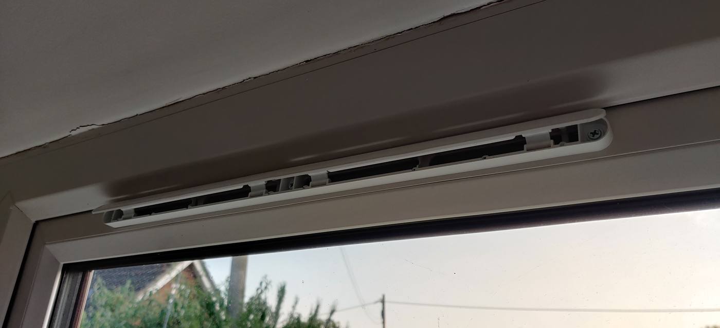 An open trickle vent built into the top of a window frame, close up