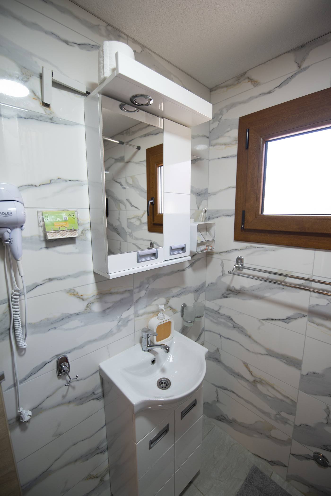 A bright, compact bathroom with a mirrored wall cabinet, small vanity and window