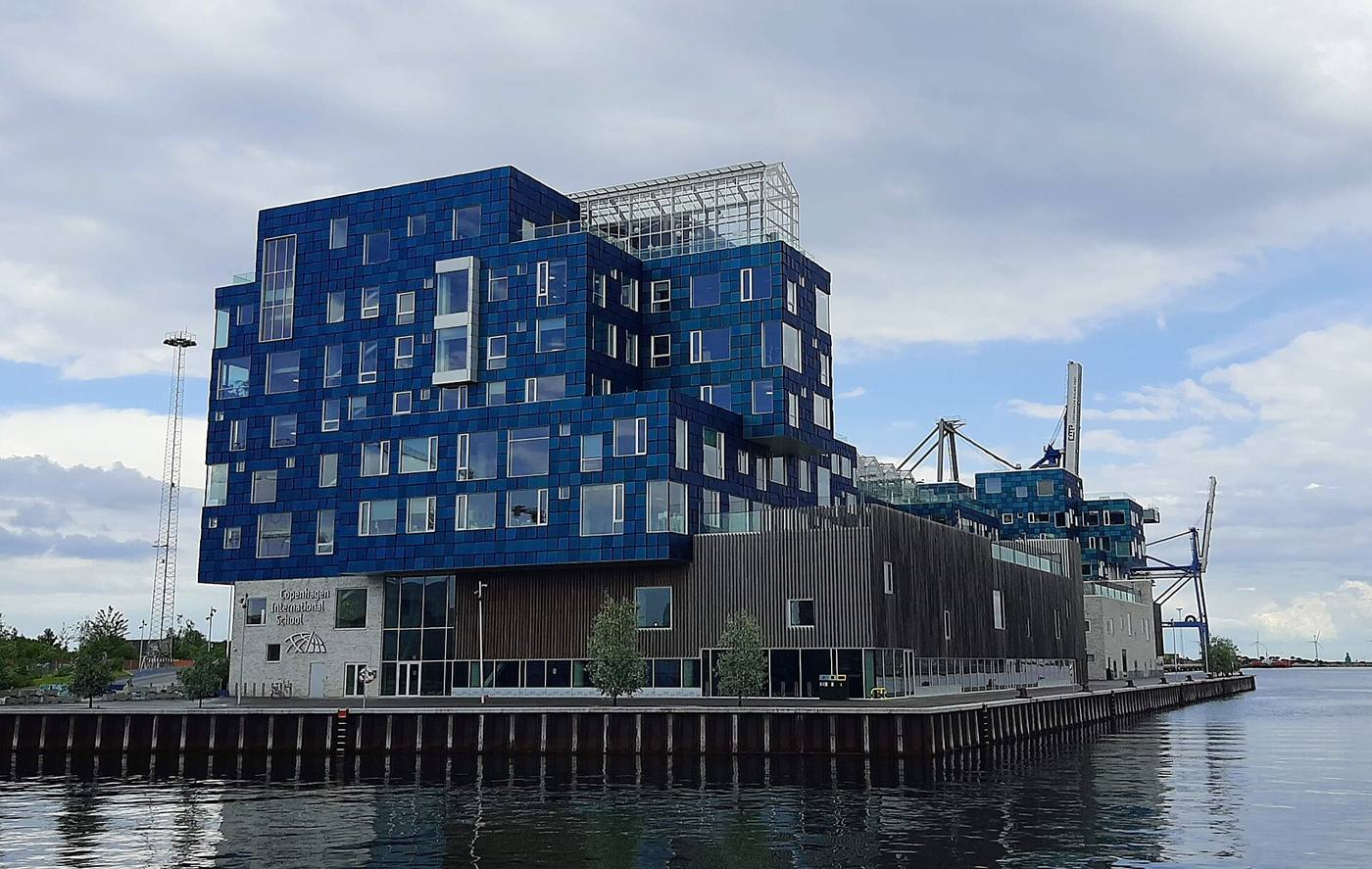 Coloured solar panels forming the sea-green photovoltaic facade of Copenhagen International School on a bright day