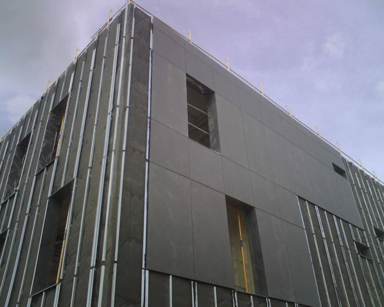 A ventilated rainscreen facade under construction, showing the support frame and cavity behind the cladding