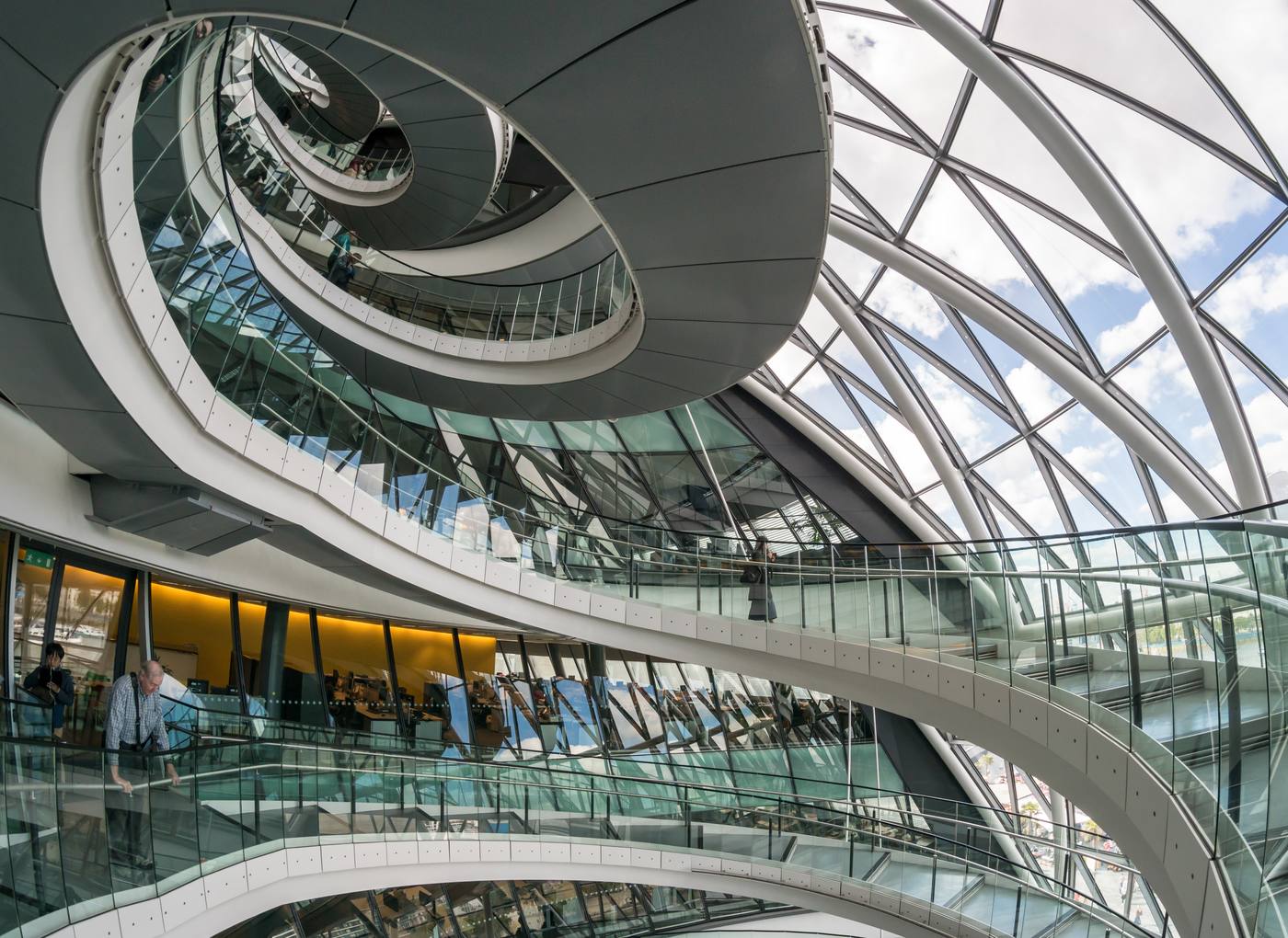 A wide spiral staircase curving upward with metal balustrade and daylight from above, inside City Hall, London