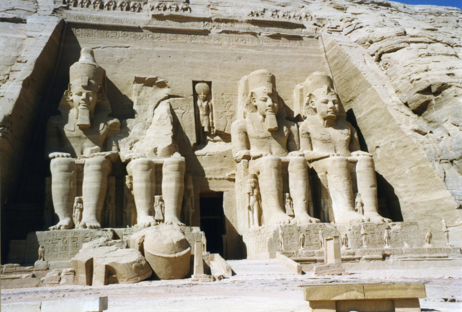 The facade of the Great Temple of Ramesses II at Abu Simbel: four colossal seated statues of the king cut from the cliff, one statue's head fallen before the entrance