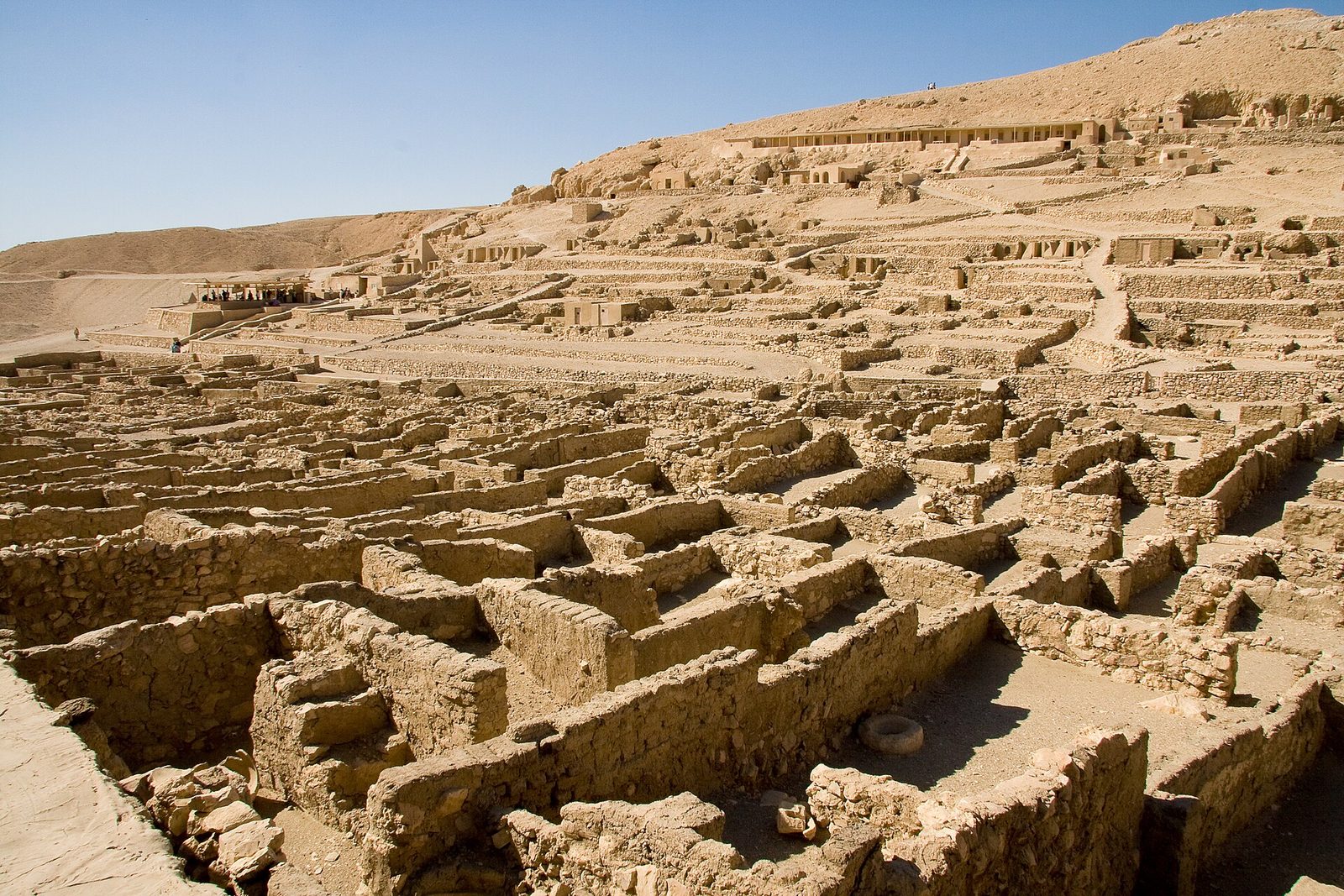The ruins of the workmen's village at Deir el-Medina: rows of stone house foundations in a desert valley below the Theban hills
