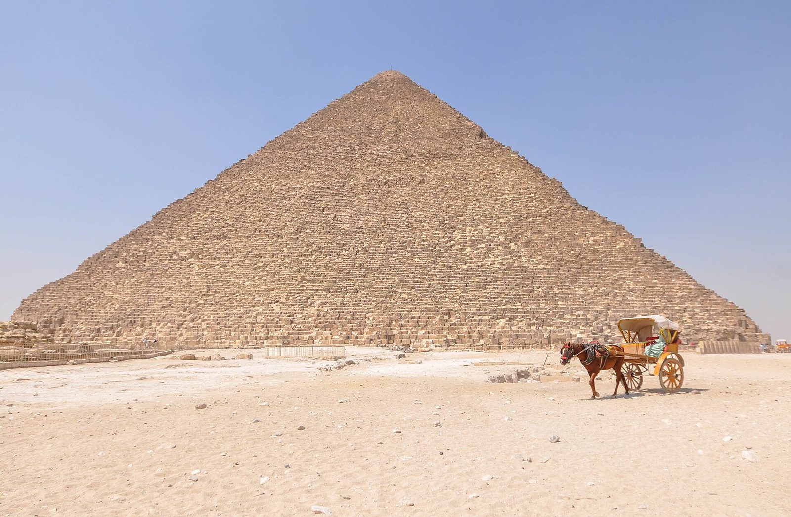 The Great Pyramid of Khufu at Giza: the stripped limestone core rising from the plateau, a horse-drawn carriage in the foreground giving the scale