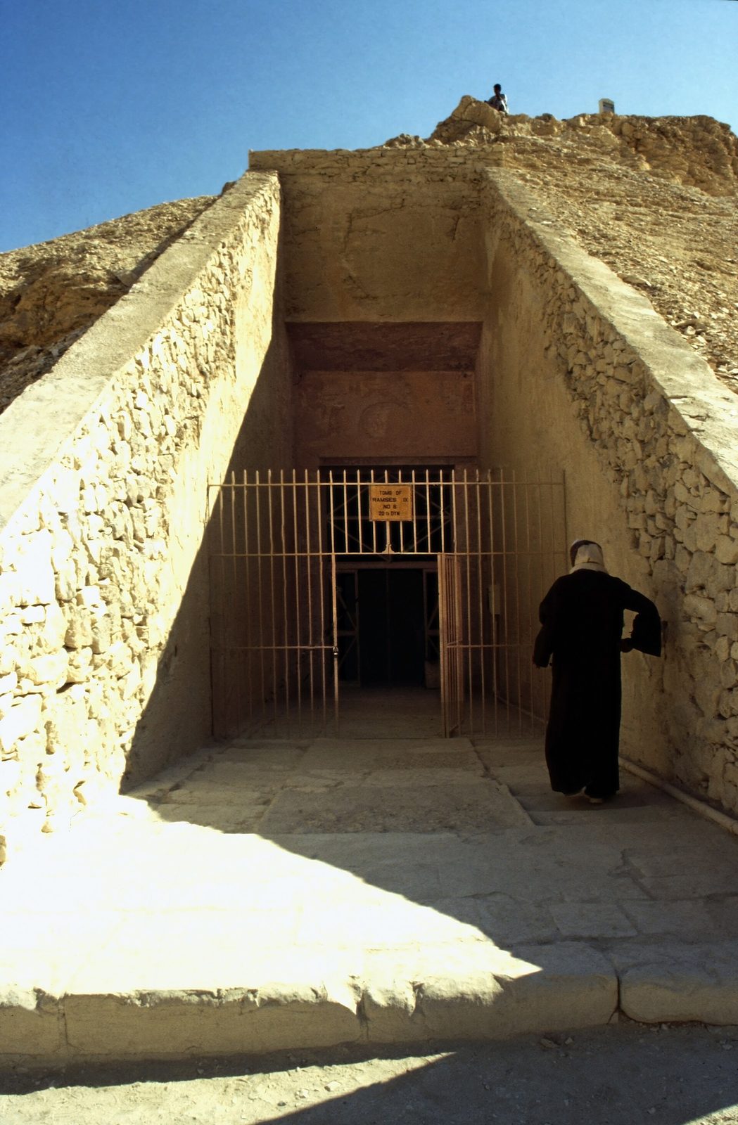 The entrance ramp of a royal tomb in the Valley of the Kings: a rock-cut stair descending between rough walls to the gated doorway