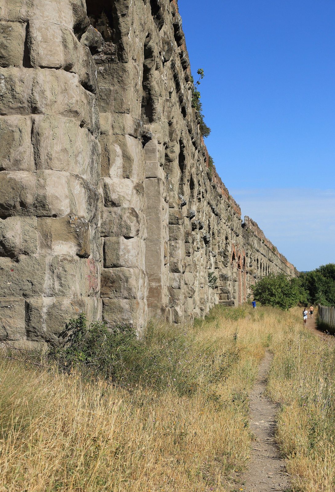 The Aqua Claudia aqueduct in Rome's Aqueduct Park: the great stone arcade seen from below at ground level, stretching away across dry grass