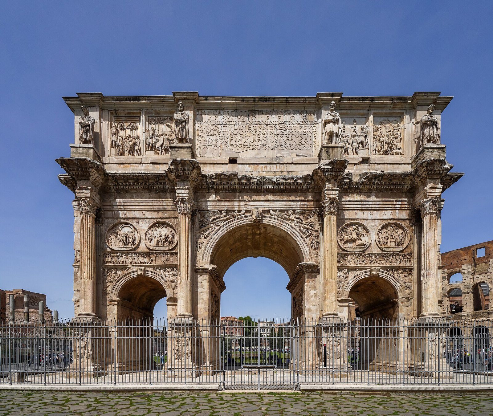 The Arch of Constantine in Rome from its south side: the triple-bayed marble arch covered in roundels and relief panels, the Colosseum just visible behind