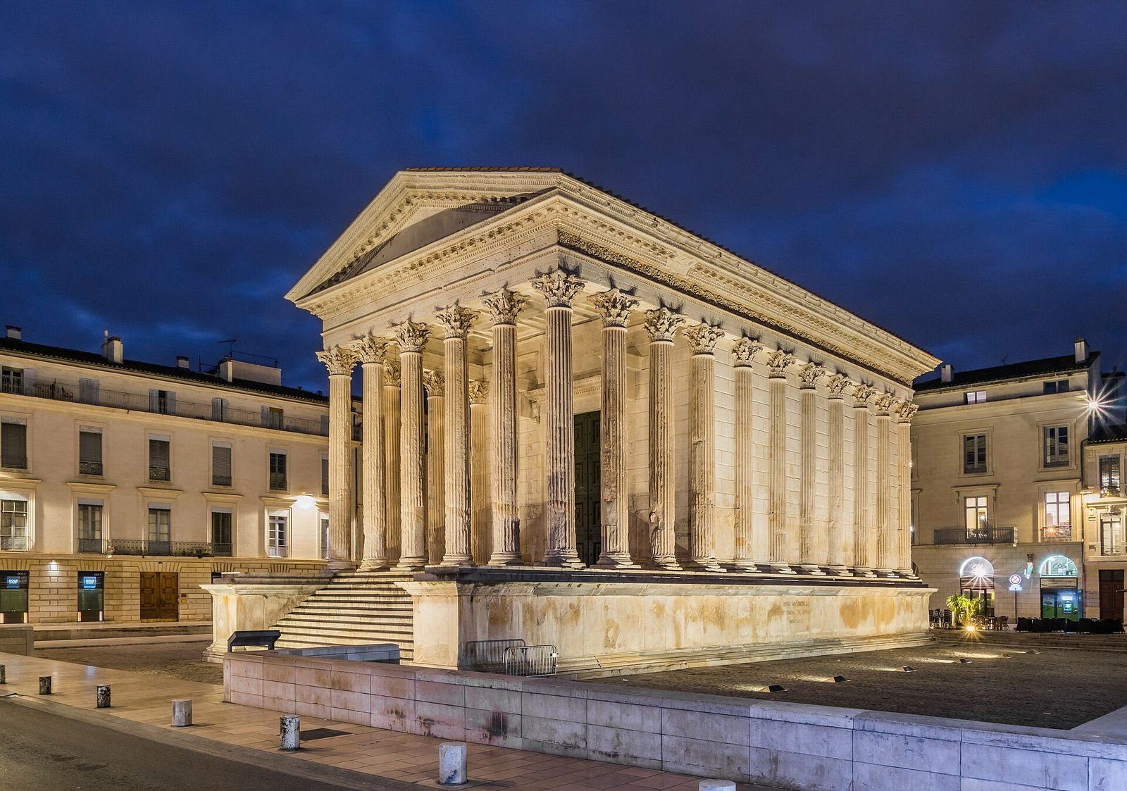 The Maison Carrée at Nîmes at dusk: the marble temple on its high podium, its Corinthian colonnade lit warmly against the evening sky