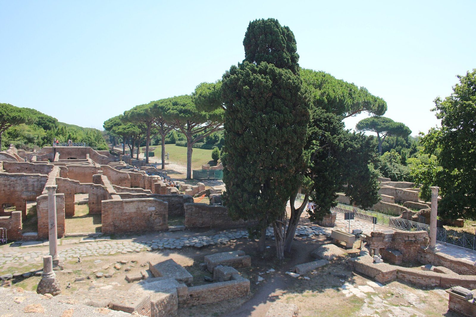 The ruins of Ostia Antica around the Decumanus Maximus: brick house walls, paved streets and umbrella pines seen from the theatre quarter