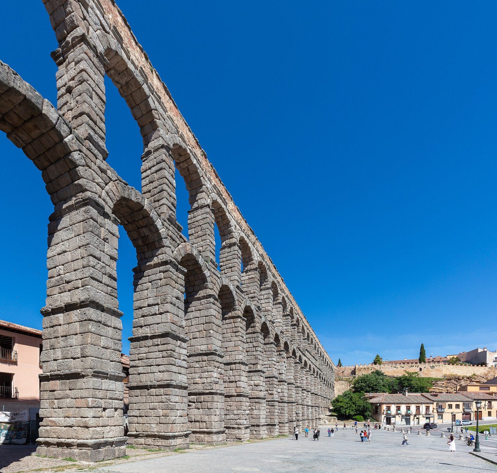 The Aqueduct of Segovia in Spain: two tiers of unmortared granite arches marching across the city square under a blue sky