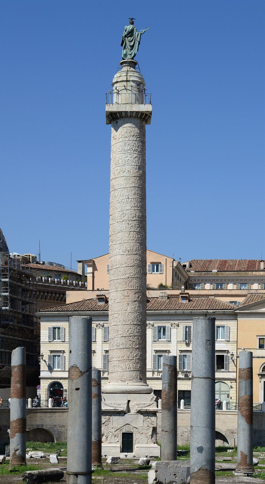 Trajan's Column in Rome at full height: the spiral relief band winding up the marble shaft to the statue at its top, with columns of the Basilica Ulpia in the foreground
