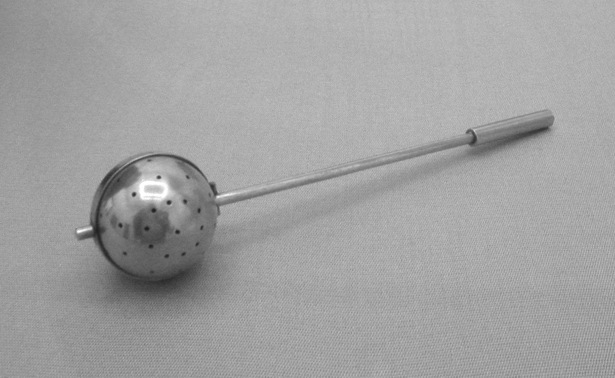 A tea infuser made in the Bauhaus metal workshop, its metal strainer and stand