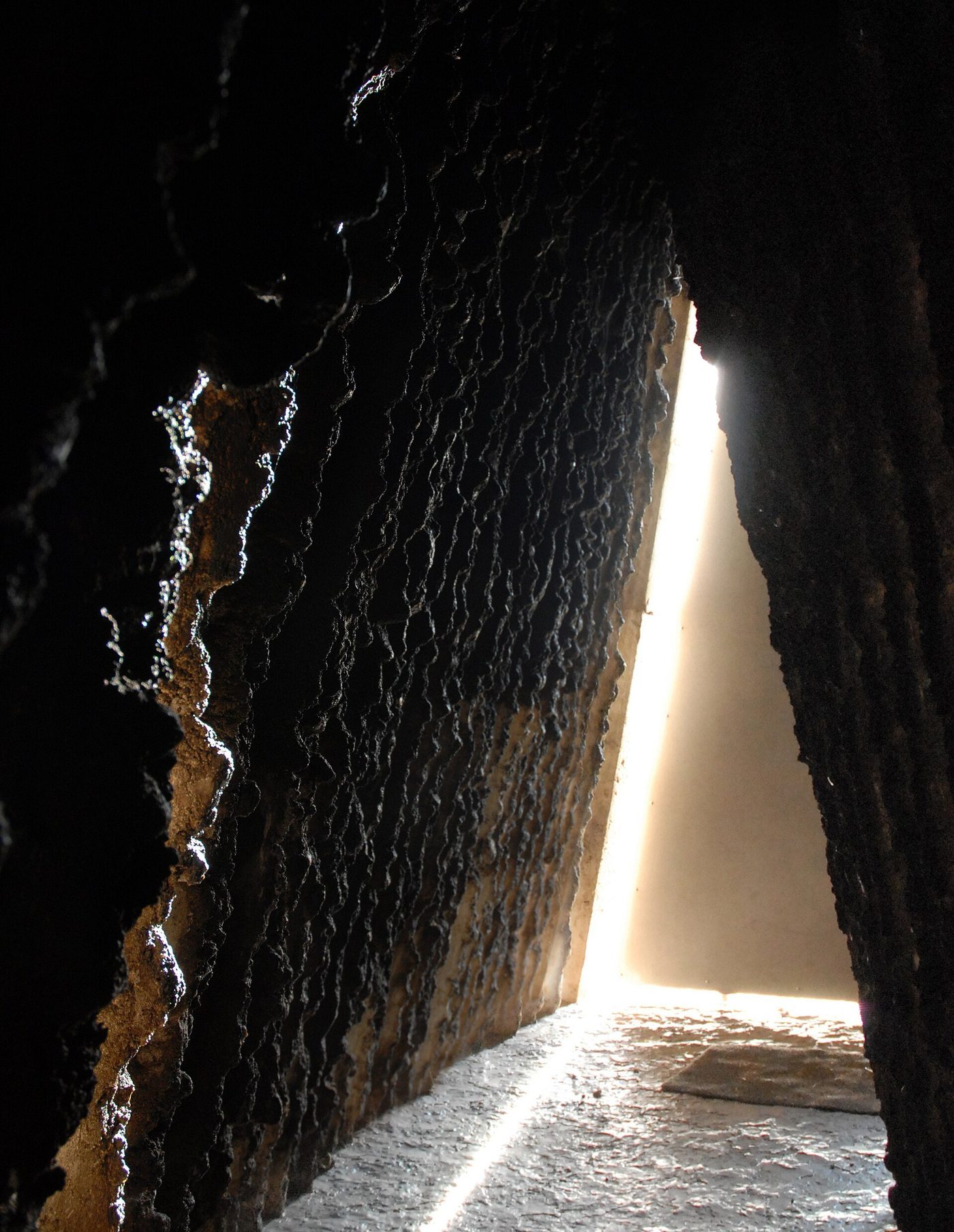 Rough cast-concrete wall with a narrow slit of light — the interior of a concrete chapel by Peter Zumthor