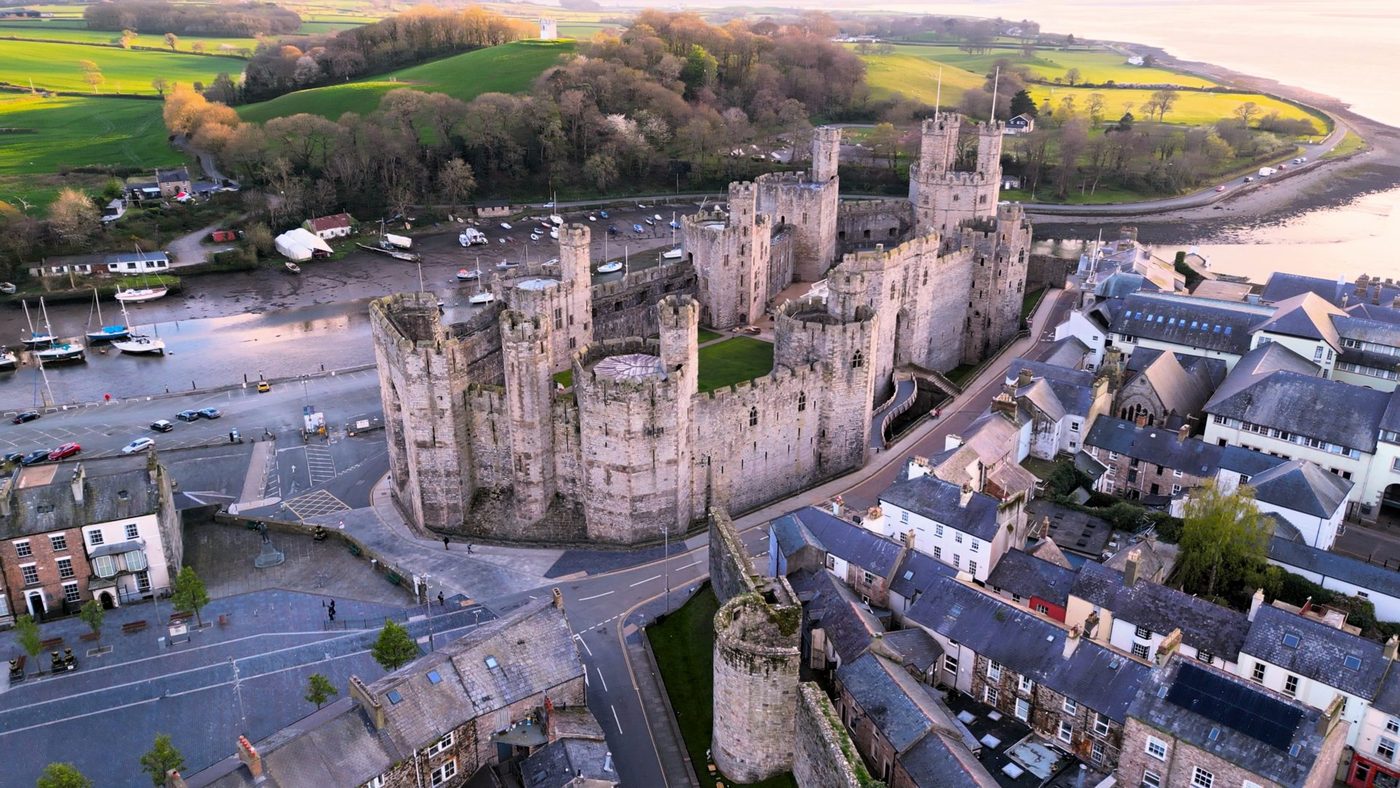 Caernarfon Castle at dusk: polygonal towers and banded masonry above the harbour