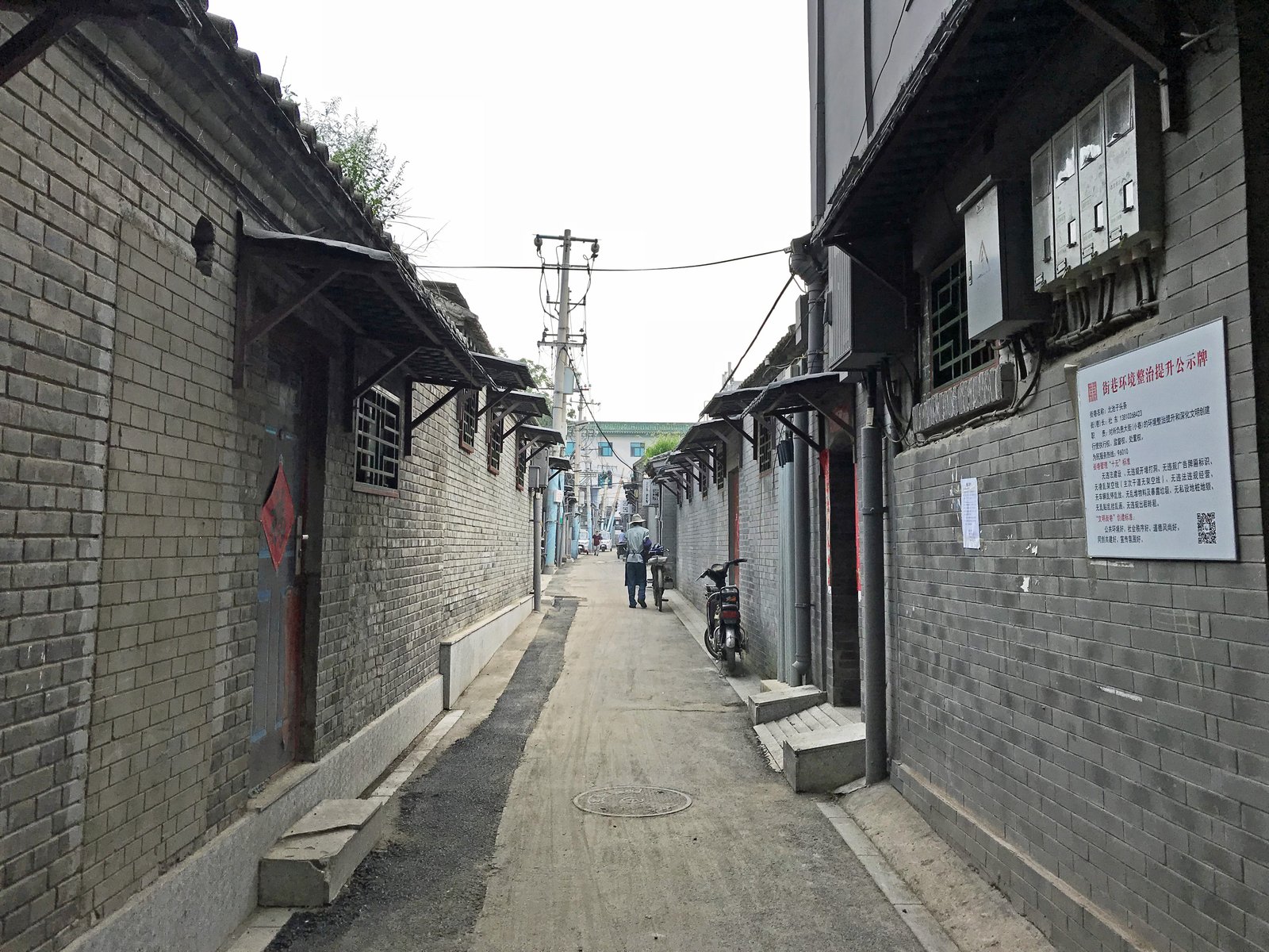 A narrow grey-brick hutong lane in Beijing, lined with courtyard-house walls
