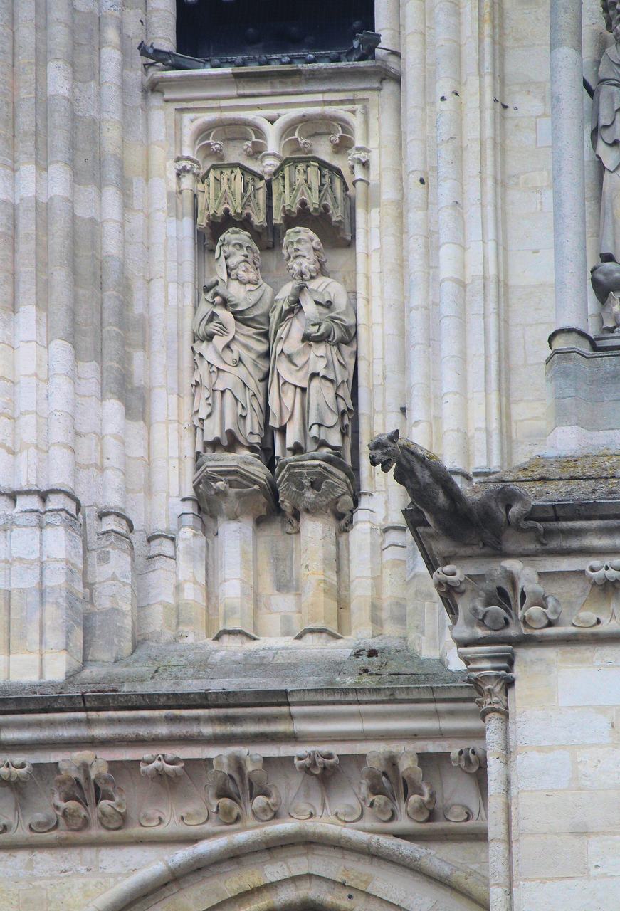 Detail of the west front sculpture of Amiens Cathedral: two standing figures and a gargoyle in weathered stone