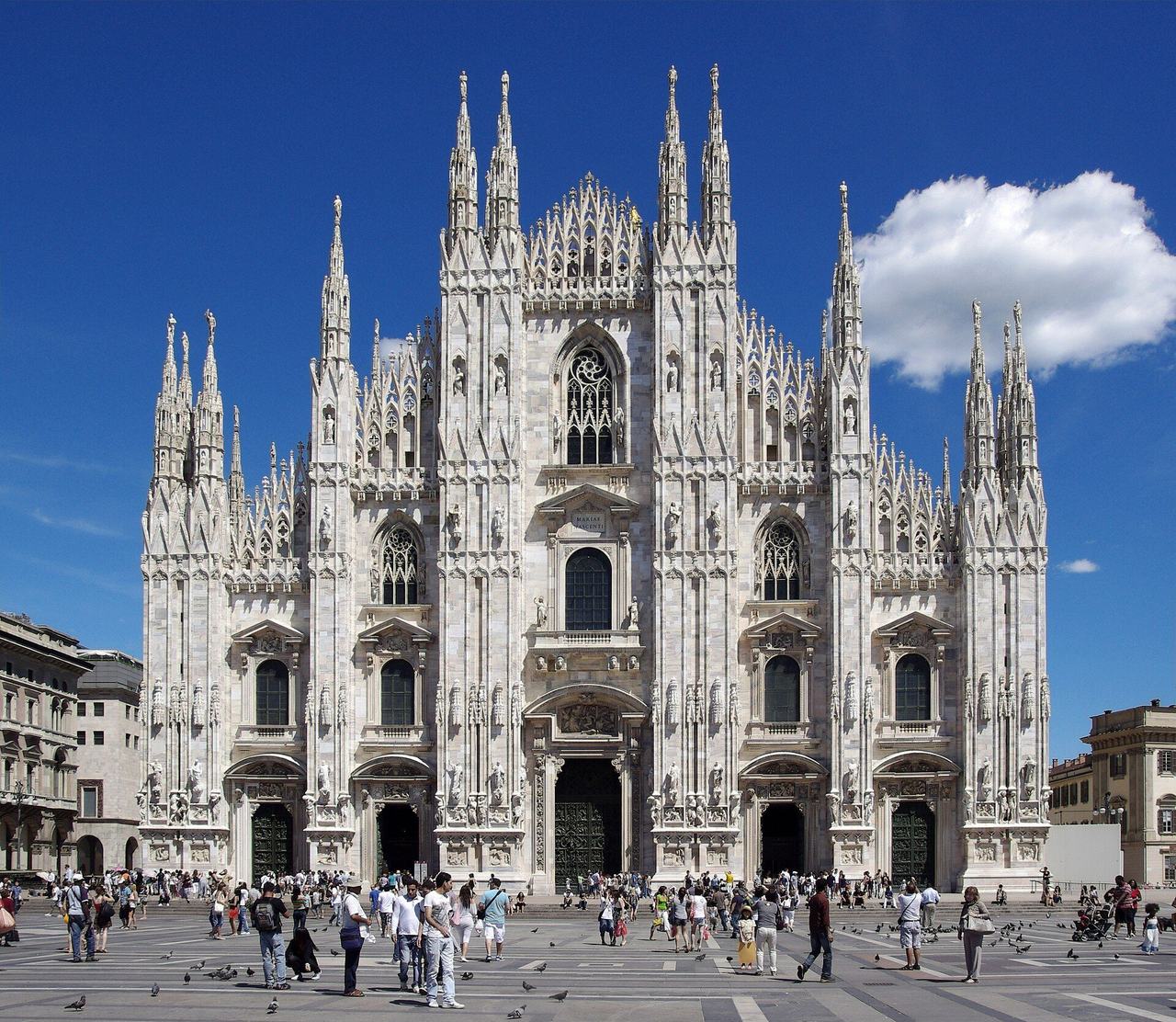 The marble facade of Milan Cathedral crowded with pinnacles, statues and traceried windows under a blue sky