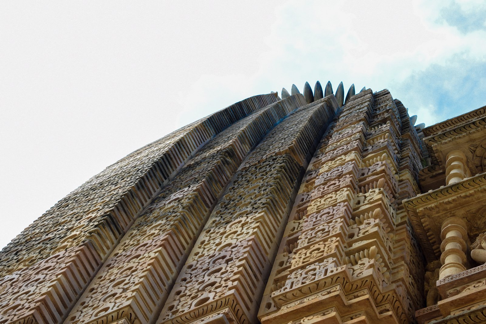 The ribbed stone shikhara of a Khajuraho temple seen from below, its curved profile rising against the sky