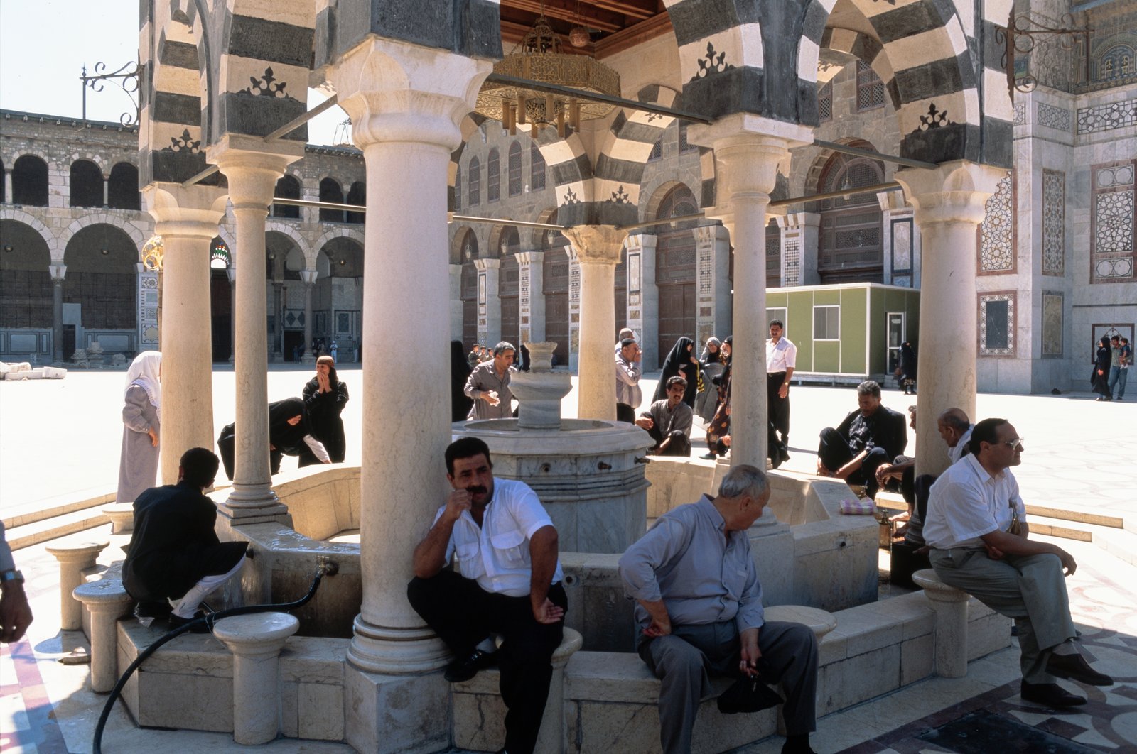 A mosque courtyard with arcades and a fountain for ablution