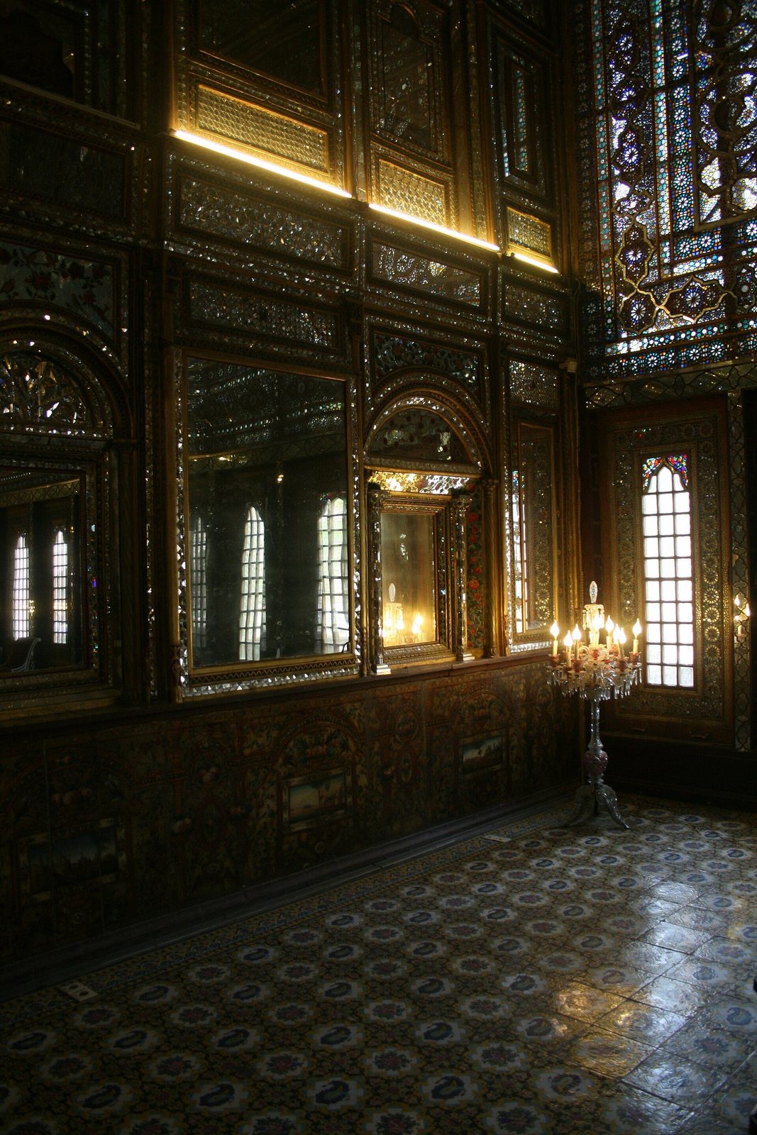 An interior of the Golestan Palace in Tehran: carved and mirrored panelling and stained glass in low light