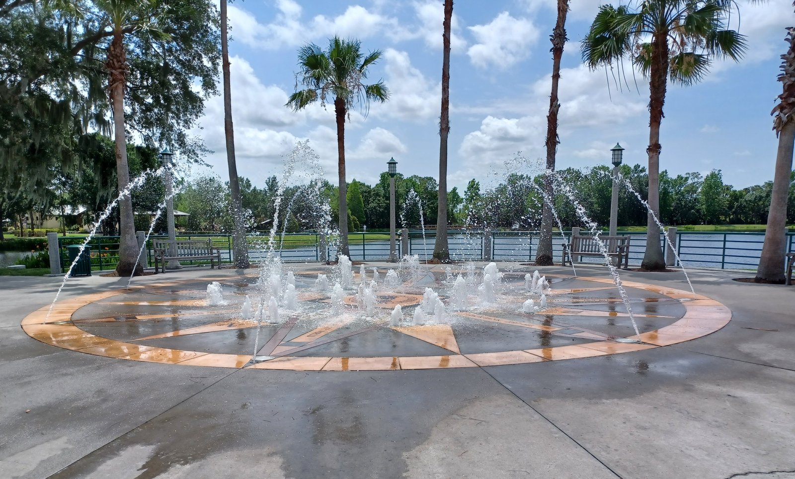 The fountain plaza in the town centre of Celebration, Florida, with water jets, palm trees and a lake behind.