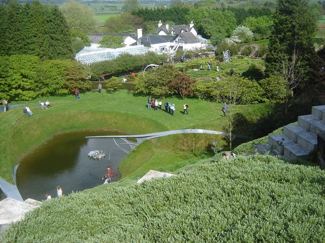 The Garden of Cosmic Speculation at Portrack in Scotland, with a pond, lawns, a bridge and the house in the distance.