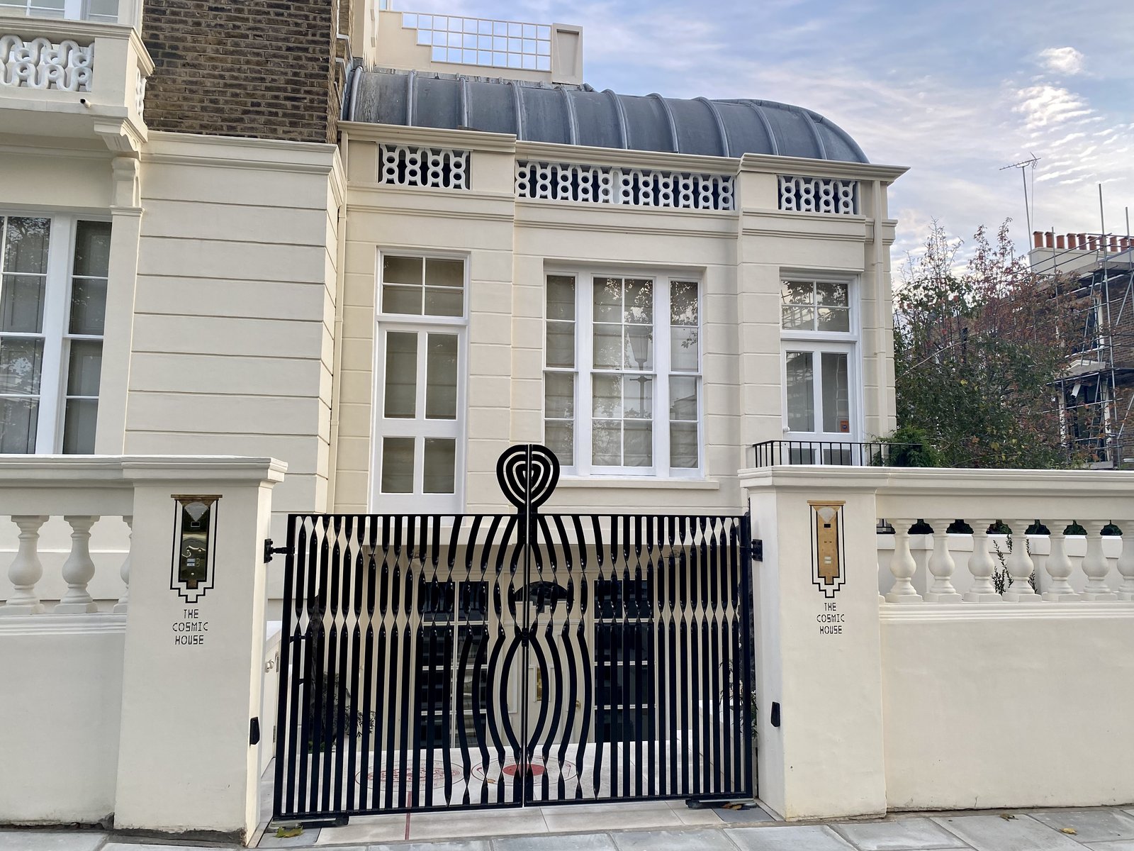 The front of Charles Jencks's Thematic (Cosmic) House in London, a white house with a curved roof behind a black iron gate.
