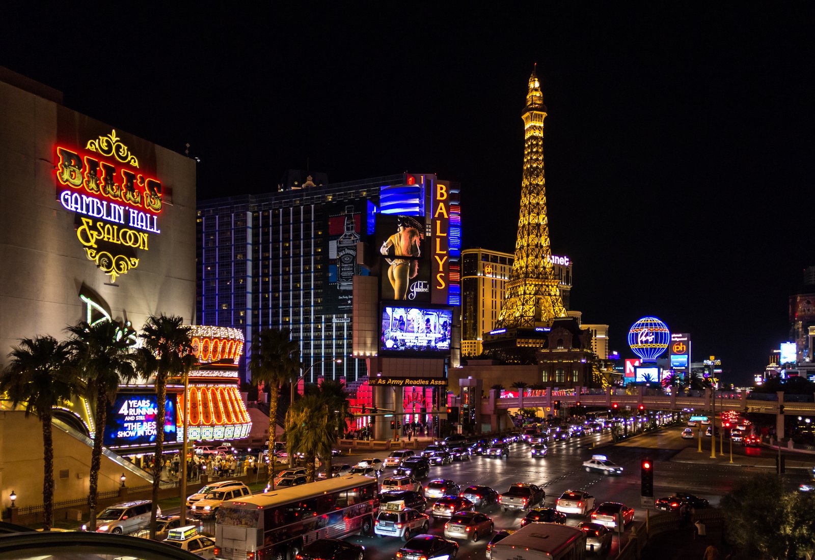 The Las Vegas Strip at night, crowded with traffic, neon signs and an illuminated Eiffel Tower replica.