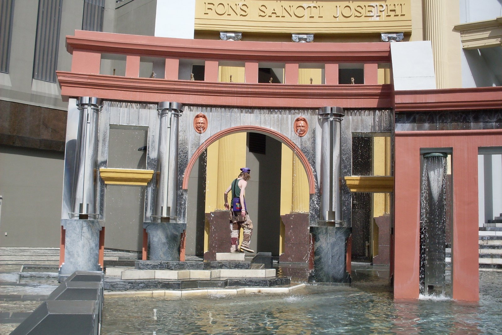 Applied ornament at Piazza d'Italia in New Orleans, including a red-framed arch, face masks and a Latin inscription above.