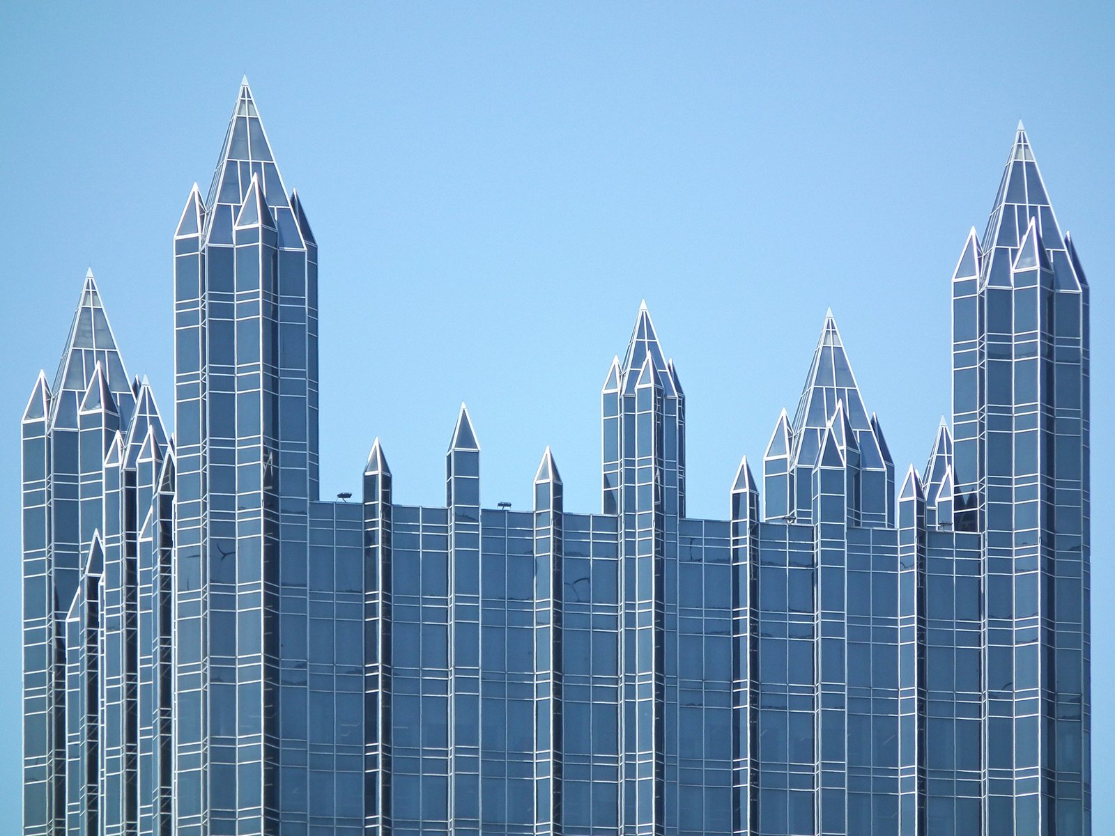 The glass spires and pointed crown of One PPG Place in Pittsburgh against a clear blue sky.