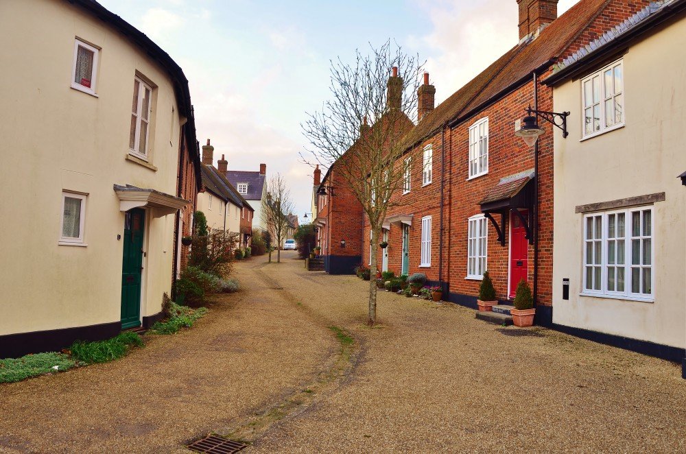 A quiet residential street in Poundbury, Dorchester, lined with brick and rendered houses in traditional styles.