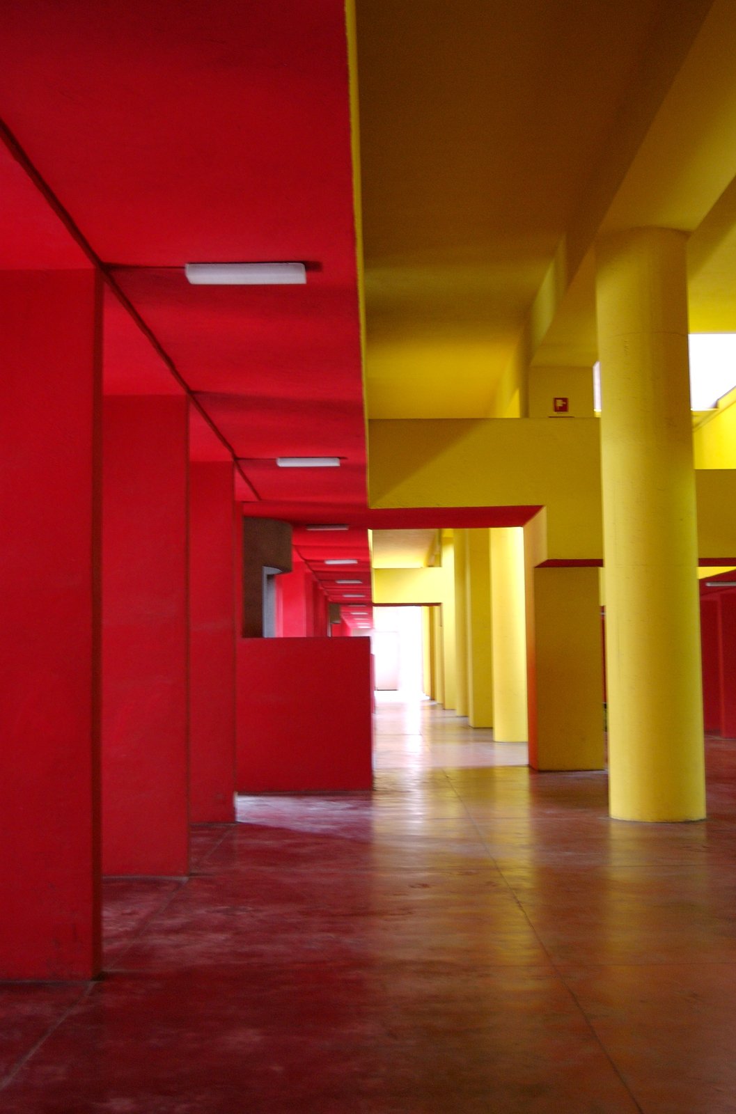 The covered internal gallery of the Gallaratese Monte Amiata housing in Milan, with bold red walls and yellow columns.