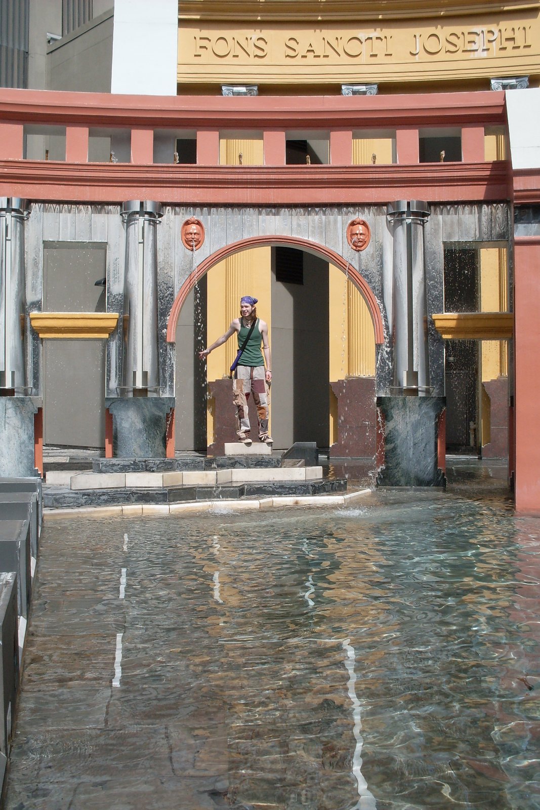 A brightly coloured arcade at Piazza d'Italia in New Orleans, with red and grey columns, a painted arch and water in the foreground.