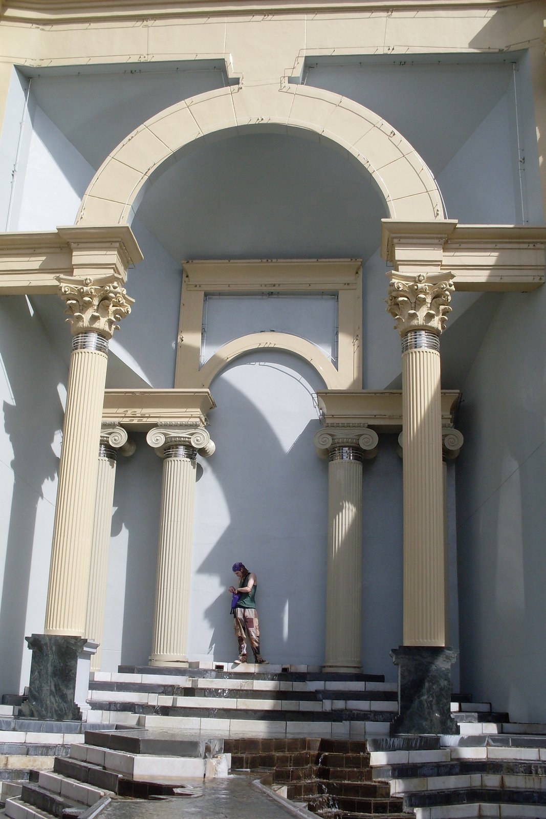 Classical columns and an arched niche at Piazza d'Italia in New Orleans, with a small figure standing on the steps below.