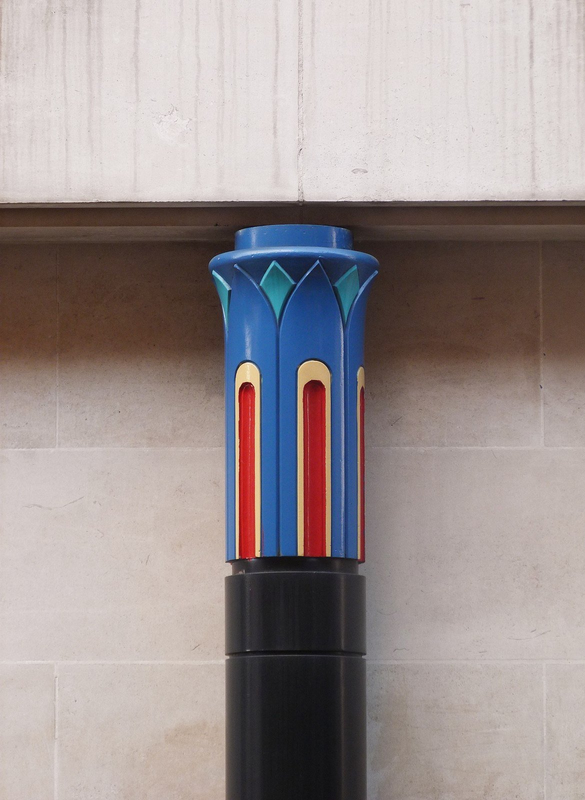 A colourful postmodern column capital at the Sainsbury Wing in London, painted blue and red against plain stone.