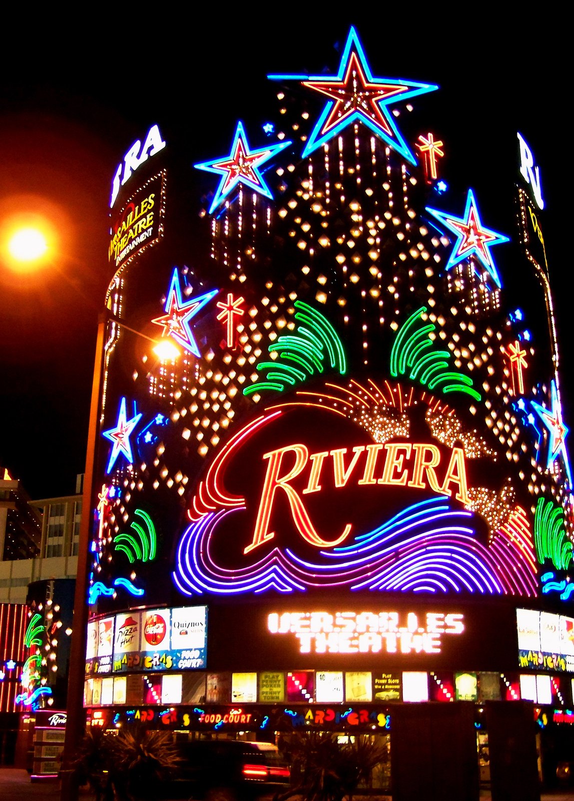 The Riviera hotel and casino in Las Vegas at night, its curved facade covered in neon stars and a large glowing Riviera sign.