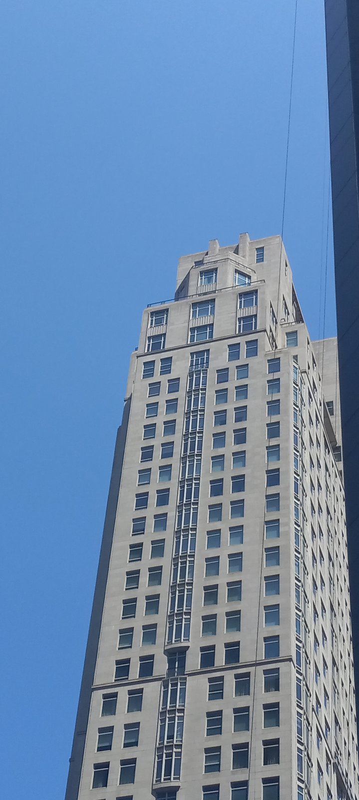 The upper tower of 15 Central Park West in New York, showing its limestone grid of windows and stepped crown against the sky.