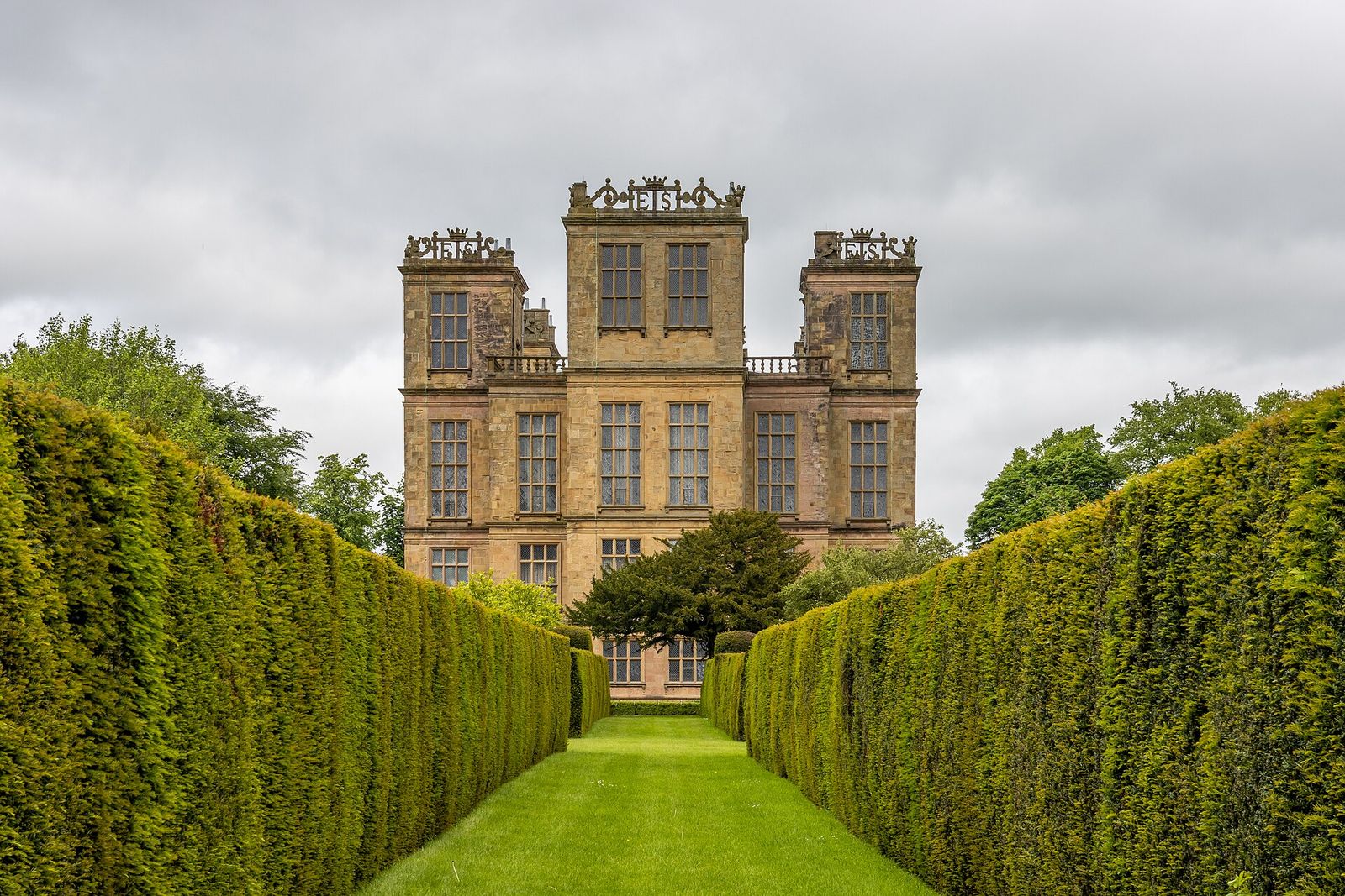 Hardwick Hall in Derbyshire seen from its garden, a many-windowed stone house between high hedges