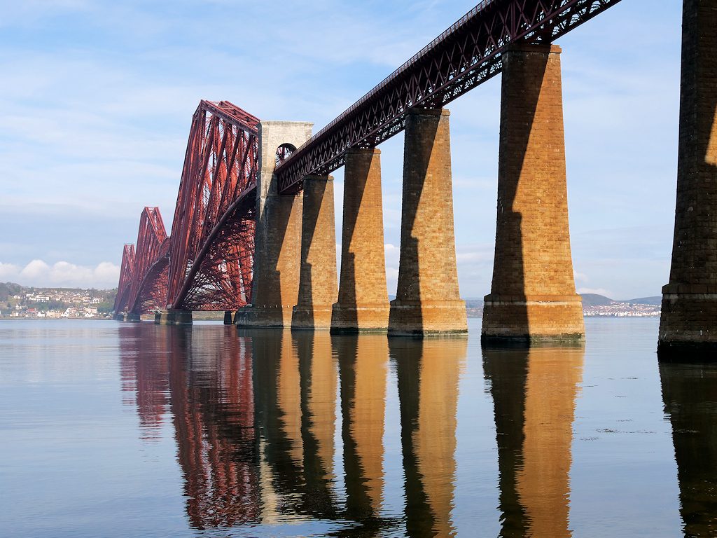 The Forth Bridge from South Queensferry: the steel cantilevers and granite piers reflected in the Firth of Forth