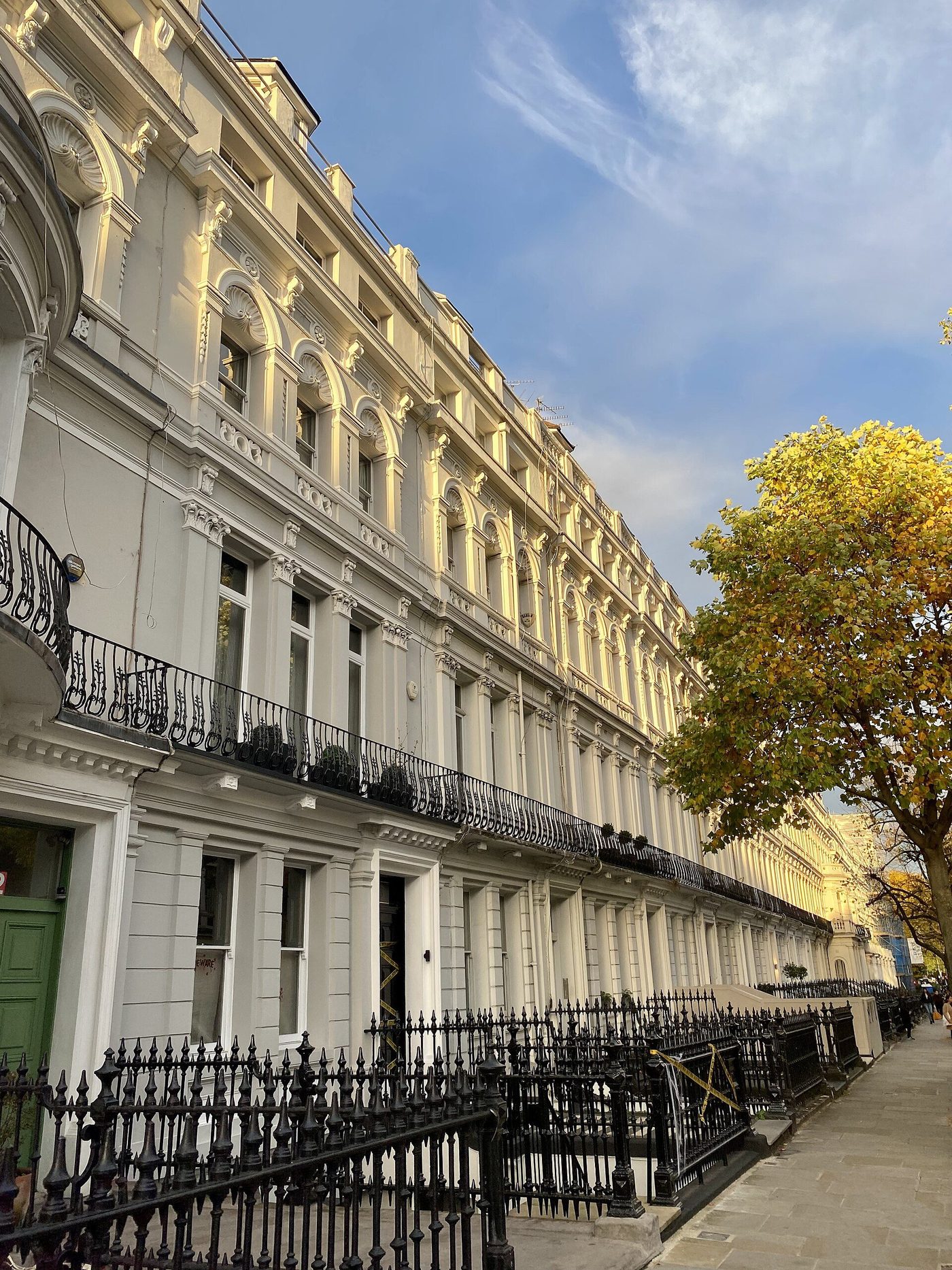 A stucco terrace in Notting Hill: white rendered fronts, iron balconies and a shared parapet line down the street