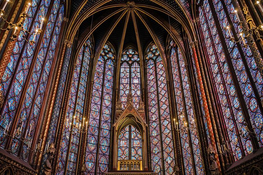 Stained glass of Sainte-Chapelle filling the wall between slender stone piers with coloured light